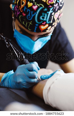 Latin woman tattoo artist demonstrates the process of getting tattoo with paint and works in blue sterile gloves in Mexico city