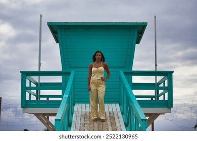 Latin woman, young and beautiful riding on the lifeguard stand on a beach in Cadiz, Spain. She is barefoot on the ramp and does different body postures. Blowing air and sea breeze - Powered by Shutterstock