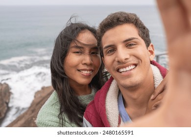 Latin young couple taking a selfie in a viewpoint enjoying beach day in winter - Powered by Shutterstock