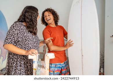 Latin young male and female colleagues laughing while working in a surfboard workshop - Powered by Shutterstock