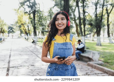 latin young woman with headphones listening music on public park in Mexico Latin America, hispanic girl - Powered by Shutterstock