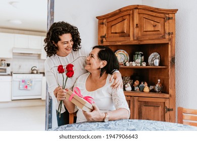 Latin Young Woman And Her Mother Middle Age With Flowers And Gift Box At Home Celebrating Happy Mother's Day In Mexico City