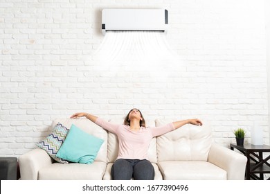 Latin Young Woman Relaxing Under Mini Split On Sofa In Living Room At Home