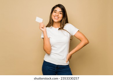 Latin young woman wearing a white mock-up t-shirt with copy space holding a credit card for shopping