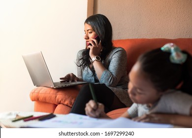 Latin Young Woman Working At Home Calling With The Mobile Phone Using The Laptop While Her Daughter Are Doing The Homework. Telecommuting Concept During Covid Infection.