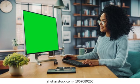 Latina Female Specialist Working on Desktop Computer with Green Screen Mock Up Display at Home Living Room while Sitting at a Table. Freelancer Female Chatting Over the Internet on Social Networks. - Shutterstock ID 1959089260