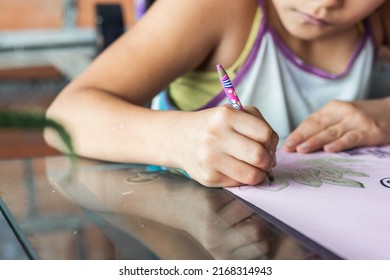 Latina Girl With Brown Skin, Coloring Her Drawing Of Green Leaves On A Cardboard For An Exhibition At Her School. Poor Student Of Limited Economic Resources Drawing With Her Colored Pencils.