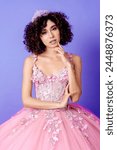 Latina girl in a pink quinceañera dress poses as a model in studio with purple background. Styled curls, subtle makeup. Close up photo.