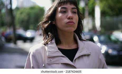 A Latina Hispanic Woman Walking In City Street With Serious Expression. South American Thoughtful Girl Walks In Sidewalk