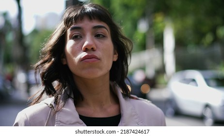 A Latina Hispanic Woman Walking In City Street With Serious Expression. South American Thoughtful Girl Walks In Sidewalk