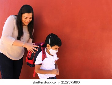 Latina Mom Prepares Her Son With A Face Mask To Protect Against Coronavirus And A Backpack For The Return To School In The New Normality Due To The Covid-19 Pandemic
