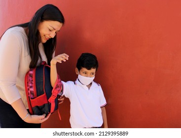 Latina Mom Prepares Her Son With A Face Mask To Protect Against Coronavirus And A Backpack For The Return To School In The New Normality Due To The Covid-19 Pandemic
