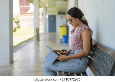 Latina student using tablet while sitting on bench at school corridor - Powered by Shutterstock - Get 15% off with code: PIKWIZARD15