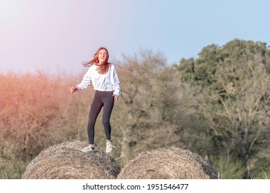 Latina Teenage Girl In Black Leggings, Top And Jacket Posing On Straw Bales In Rural Setting