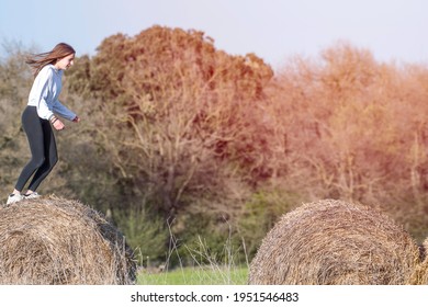 Latina Teenage Girl In Black Leggings, Top And Jacket Posing On Straw Bales In Rural Setting