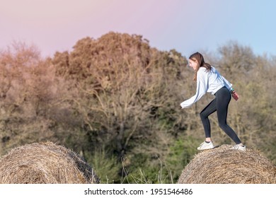 Latina Teenage Girl In Black Leggings, Top And Jacket Posing On Straw Bales In Rural Setting