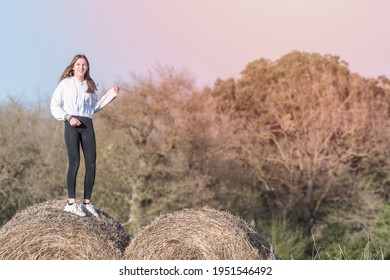 Latina Teenage Girl In Black Leggings, Top And Jacket Posing On Straw Bales In Rural Setting