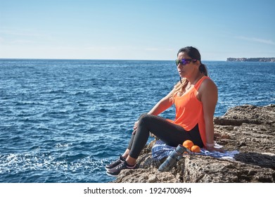 Latina Woman, 30 To 50 Years Old, Meditating And Resting On A Cliff, Relaxing With The Sea, With A Bottle Of Water And Fruit,