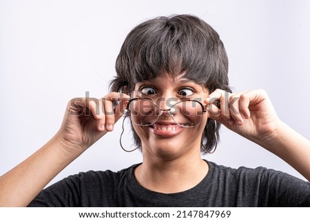 Latina woman holding her glasses while making funny faces on a white background