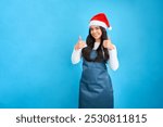 Latina woman with Santa hat and apron thumbs up in studio 