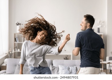 Latina woman shakes head, her hair flows wildly in energetic dance, move to music with husband in living room, family have blast at party on weekend in modern apartment. Hobby, fun, recreation at home - Powered by Shutterstock