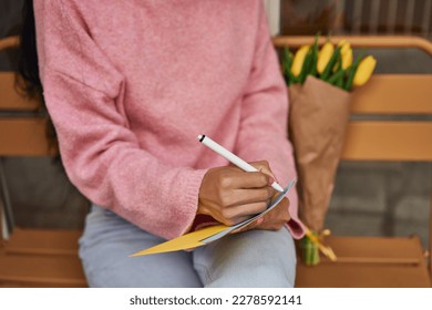 Latina woman writing love letter with yellow tulips.