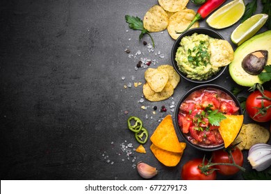 Latinamerican Mexican Food Party Sauce Guacamole, Salsa, Chips And Ingredients On Black Table. Top View Copy Space.