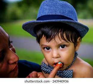 Latino Baby Wearing A Blue Hat And Bow Tie Eating Frosting From His Mother's Finger