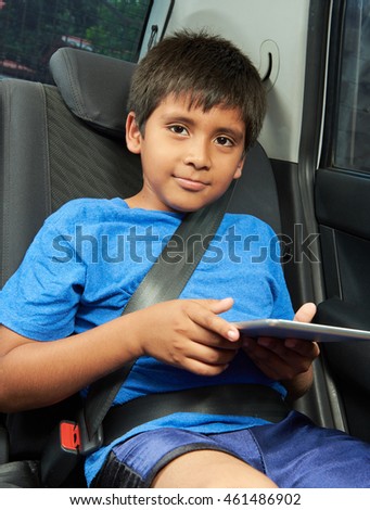 latino boy with tablet in back seat of car