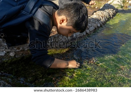 Latino boy taking algae sample during school field trip to explore ecosystem sustainability
