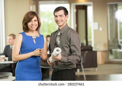 Latino Business Man And Woman Holding Blueprints And Building Designs