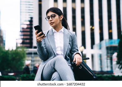 Latino Businesswoman Reading Financial News On Web Page Via Cell Smartphone, Confident Female CEO Using Mobile Phone For Search Contact Number Or Data Info During Work Break At Urban Setting