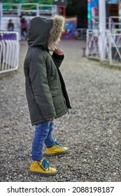 Latino Child Dressed In Jeans And Green Parka In Fur Hood Lost In An Amusement Park. Wintertime, Vertical