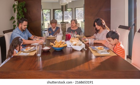 Latino Family Sitting At The Dining Room Table Giving Thanks For The Food.