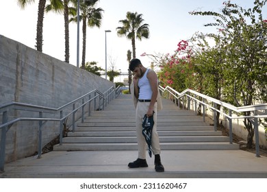 Latino and Hispanic boy, young and nonconformist, rebellious, with jacket on his shoulder and looking at the ground, sad and regretful. Problematic concept, rebellion, gangs. - Shutterstock ID 2311620467