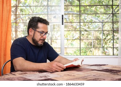 A Latino man living with HIV sitting at his dining room table reading a book - Powered by Shutterstock