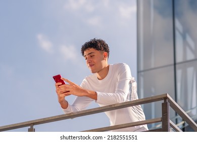 Latino Man In Sportswear Leaning On The Fence Of The Stairs Texting On His Cell Phone After His Workout. Healthy Lifestyle. 