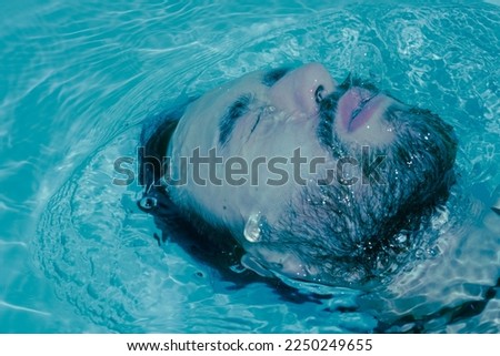 Latino man submerged in water pulling his face out drowning, struggles against water