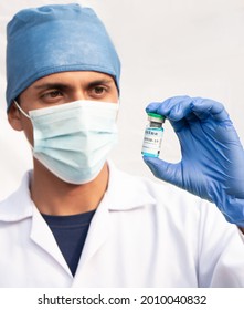 Latino Nurse Holding A Vial Containing A Blue Liquid, Covid19 Vaccine. Hispanic Man On White Background.