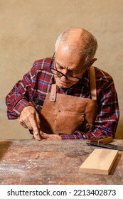 Latino Senior Man And Concentrated Skilled Carpenter Sharpening His Pencil With A Chisel