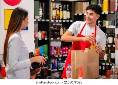 Latino Worker Attends To A Customer In A Supermarket Placing The Groceries In The Bag.