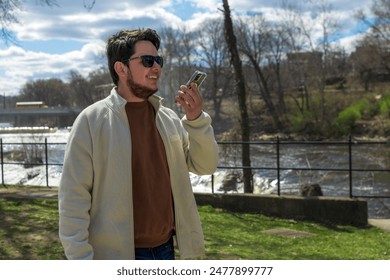 Latino young adult having a call on his vacation time, Paterson waterfalls background - Powered by Shutterstock