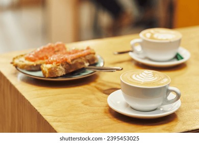 Latte with art on a wooden table, accompanied by a plate of bread with tomato - Shutterstock ID 2395453025