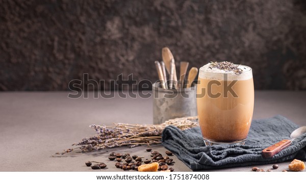 Latte or cappuccino with milk foam\
and lavender in a glass with coffee beans. Dark\
background