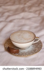 Latte Coffee In Beautiful Porcelain Cup On Bed Sheets