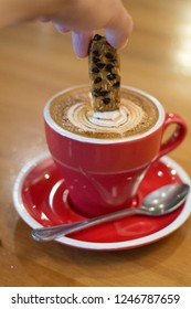 latte coffee with biscotti and latte art in red cup and saucer