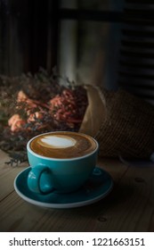 Latte coffee cups placed on a wooden table with a bouquet of dried flowers placed next to.