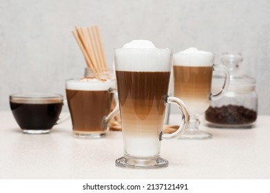 Latte macchiato with foam on the table against the background of cups with coffee, cappuccino 