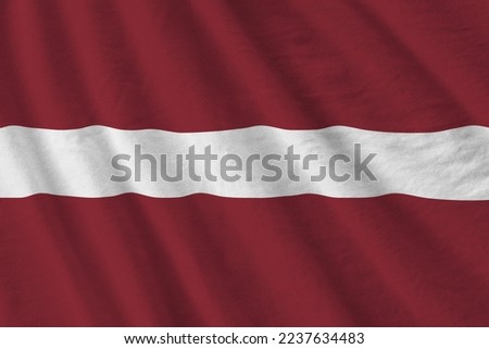 Latvia flag with big folds waving close up under the studio light indoors. The official symbols and colors in fabric banner