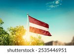 Latvia national flag waving in blue sky behind the tree and building. The flag blowing with beautiful sunlight. Latvia national flag for independence day.